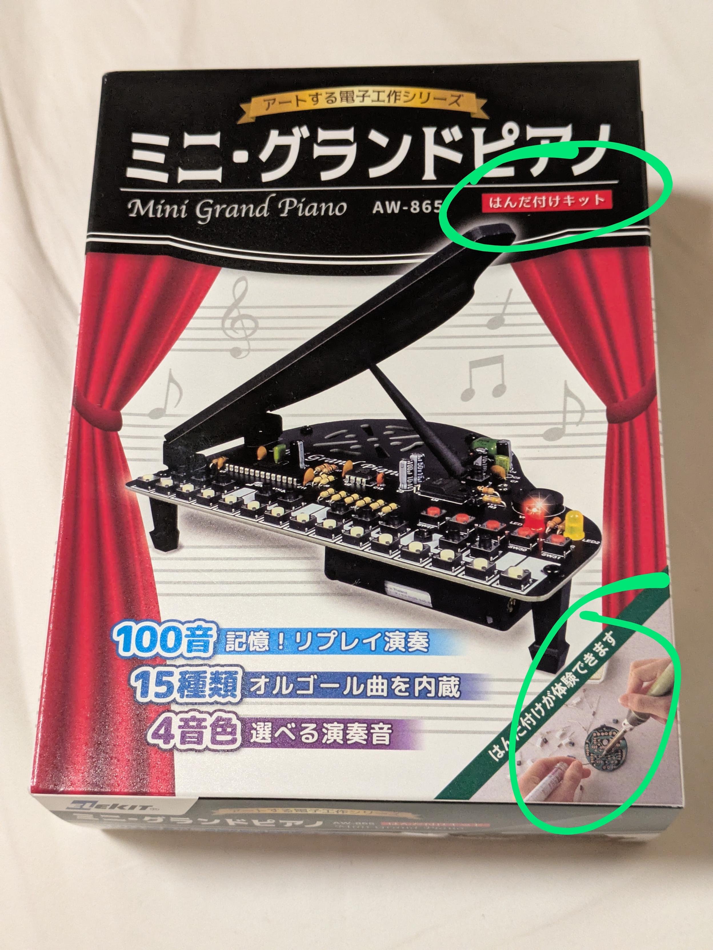 An electronics kit box for a mini grand piano. The text "soldering kit" in Japanese is visible in an eye-catching red, and the corner shows a photograph of a pair of hands soldering a board.